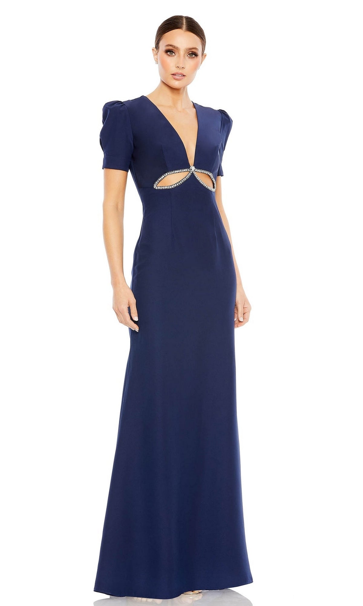 A woman in the Mac Duggal 2630 evening gown—a floor-length, navy blue formal dress with short puff sleeves, a plunging neckline, midriff cutout, and small embellishments.